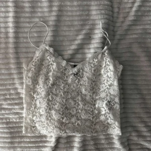 Vit spetslinne - Säljer ett sött vitt spetslinne med smala axelband. Perfekt för varma sommardagar eller som ett lager under en kavaj. Linnet har en vacker blommig spetsdesign som ger en romantisk touch. Ni står för frakt