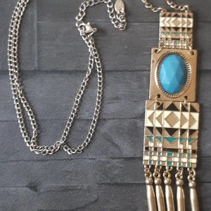 Bohemiskt halsband med turkos sten - Snyggt bohemiskt halsband med en stor turkos sten i mitten. Halsbandet har en kedja i silverfärg och detaljer i guld med geometriska mönster. Perfekt för att ge en unik touch till din outfit! Halsbandet totala längd 50 cm