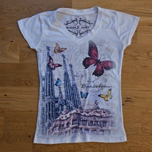 Vit t-shirt med tryck från Ikebana K Design - Säljer en superfin vit t-shirt från Ikebana K Design med ett färgglatt fjärilstryck. T-shirten har en v-ringad hals och korta ärmar🦋