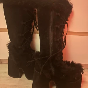 Svarta demonias - Säljer ett par svarta boots i mocka med pälsdetaljer och snörning. De har en hög klack och dragkedja på sidan för enkel på- och avtagning. Perfekta för vintern och hösten när du vill hålla dig varm och snygg. Använda men i bra skick.