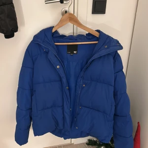 Blå pufferjacka från 157 - Säljer en snygg blå pufferjacka från 157 i storlek XS/S. Jackan är perfekt för kalla dagar med sin vadderade design och har en praktisk huva. Den är i mycket bra skick och har en dragkedja framtill. Perfekt för vintern! 💙