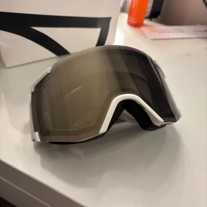 Skidglasögon från Salomon - tilrena skidglasögon från Salomon med en bred, justerbar rem i grått och vitt. Linsen är mörktonad för att skydda mot starkt solljus och ge bra sikt i backen. Använda en gång. Orginalpris 900kr säljer för 230kr⛄️ (tillhörande förvaringspåse) 