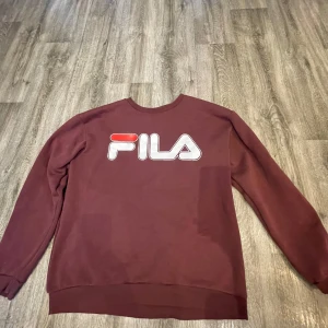 Vinröd sweatshirt från FILA - Säljer en vinröd sweatshirt från FILA med stor logga på framsidan. Tröjan har långa ärmar och rund halsringning. Perfekt för en avslappnad stil.