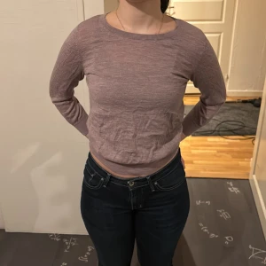 Ljuslila tröja med knappar i ryggen - Säljer en ljuslila tröja med rund hals och långa ärmar. Tröjan har en unik detalj med knappar längs ryggen. Perfekt för en stilren och bekväm look.