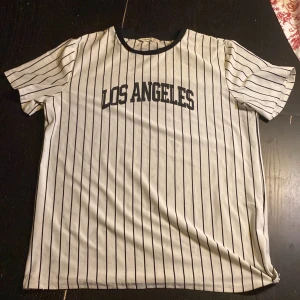 Randig t-shirt från Shein med texten 'Los Angeles' - Snygg vit och svart randig t-shirt från Shein med texten 'Los Angeles' på framsidan. Den har korta ärmar och en rund halsringning. Perfekt för en avslappnad stil.