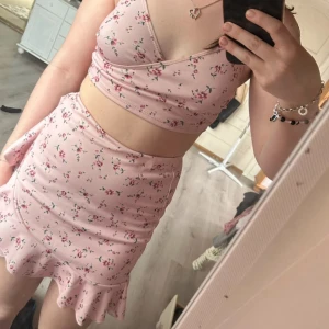 Rosa blommigt set - Säljer en superfin rosa set med blommigt mönster. Toppen har smala axelband och en omlott-design framtill. Perfekt för sommardagar eller en festlig kväll. Matcha med en kjol eller jeans för en söt look! 🌸