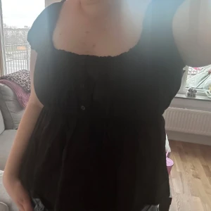 Svart blus från H&M - Säljer en svart blus från H&M med korta ärmar och en söt knappdetalj framtill. Storlek L! 