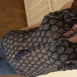 Mönstrad blus med volangdetaljer - Super säg blus med ett mörkblått och vitt mönster. Blusen har volangdetaljer längs halsen och knytning, haft på mig cirka 2 gånger och är i storlek S. Köpt i Spanien 