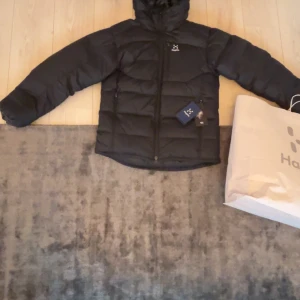 Svart dunjacka från Haglöfs - Säljer en svart vinterjacka från Haglöfs, perfekt för kalla dagar. Jackan har en dragkedja framtill och är långärmad. Den är designad för att hålla dig varm och bekväm under vintern. Helt ny aldrig använd 