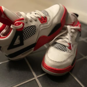 Nike Air Jordans i vitt och rött - Snygga Nike Air Jordans i vitt med röda och svarta detaljer. Skorna har snörning och en klassisk design med synlig luftdämpning i sulan. Perfekta för dig som vill ha en stilren och sportig look.