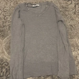 Grå v-ringad tröja - Säljer en stilren grå tröja med v-ringning. Tröjan har långa ärmar och ribbade kanter vid ärmslut och nederkant. Perfekt för en avslappnad look.