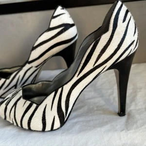 Zebramönstrade pumps från Guess - Snygga zebramönstrade pumps från Guess med hög klack och öppen tå. Perfekta för att ge en djärv touch till din outfit.