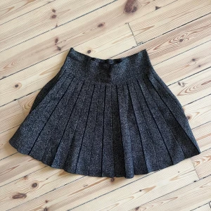 Glittrig svart kjol - Säljer en superfin glittrig svart kjol med veckad design. Perfekt för festliga tillfällen! Kjolen har en härlig glans och är i nyskick. Den är kort och passar perfekt till både vardag och fest. 🖤✨