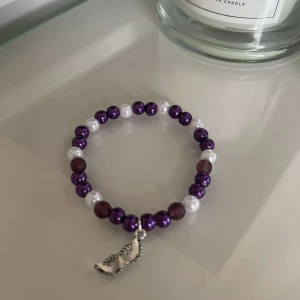 Pärlarmband med lila och vita pärlor - Säljer ett superfint armband med lila och vita pärlor. Armbandet har en söt liten silverfärgad berlock i form av en delfin. Perfekt för att ge en färgklick till din outfit! 🐬