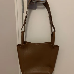 Äkta skinn handväska  - Säljs den fina väskan med sköna axel begrepp i brun färg för jag använder knappt den nu längre.Fint skick, inga repor. Nytt pris 1500 kr. Säljs den för 550 kr plus frakt  för den är äkta skinn. 31x28 cm