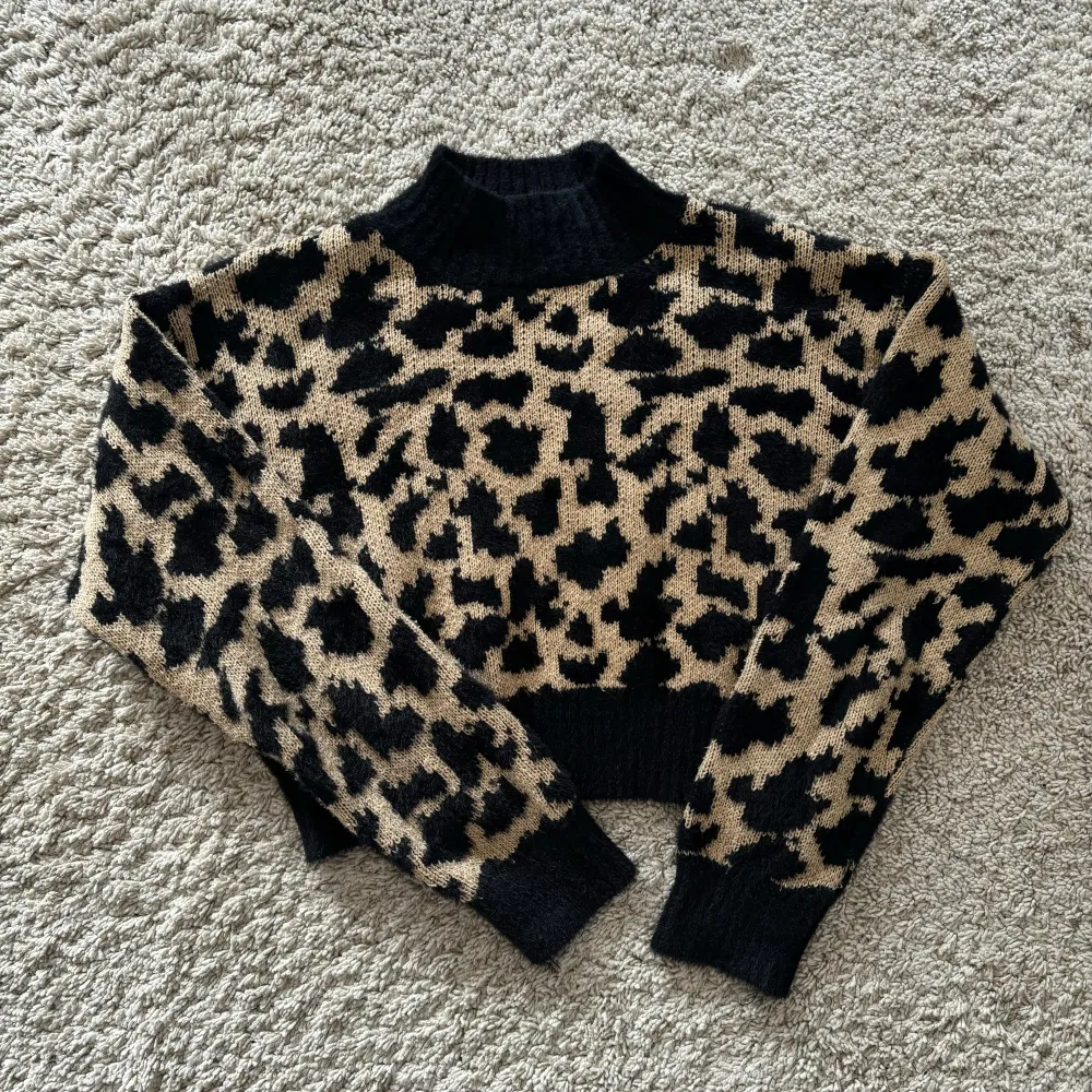 Säljer en supercool leopardmönstrad stickad tröja från NA-KD. Den är i beige och svart med en hög krage och långa ärmar. Perfekt för att hålla sig varm och snygg under hösten och vintern. Tröjan är i storlek S och är i nyskick. 🐆✨. Tröjor & Koftor.