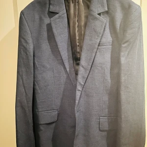 Blå kavaj från H&M - Säljer en stilren blå kavaj från H&M i storlek M. Perfekt för både formella och semi-formella tillfällen. Kavajen har en klassisk passform med två fickor framtill och en bröstficka. Materialet känns lätt och bekvämt, vilket gör den idealisk för vår och sommar.