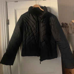 Svart quiltad jacka från Mexx - Säljer en snygg svart quiltad jacka från Mexx. Den har en dragkedja framtill och är perfekt för höst och vinter. Jackan är i nyskick och har långa ärmar. Den är både stilren och varm, perfekt för kyliga dagar!