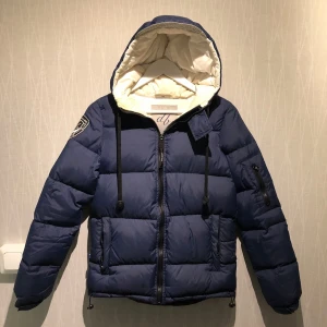 dB dunjacka - Fint skick! - Marinblå dunjacka från dBrand. Jättevarm och skön vinterjacka. Innerficka till höger. Storlek XS.  Köpt på Nelly förra hösten för 2495kr.