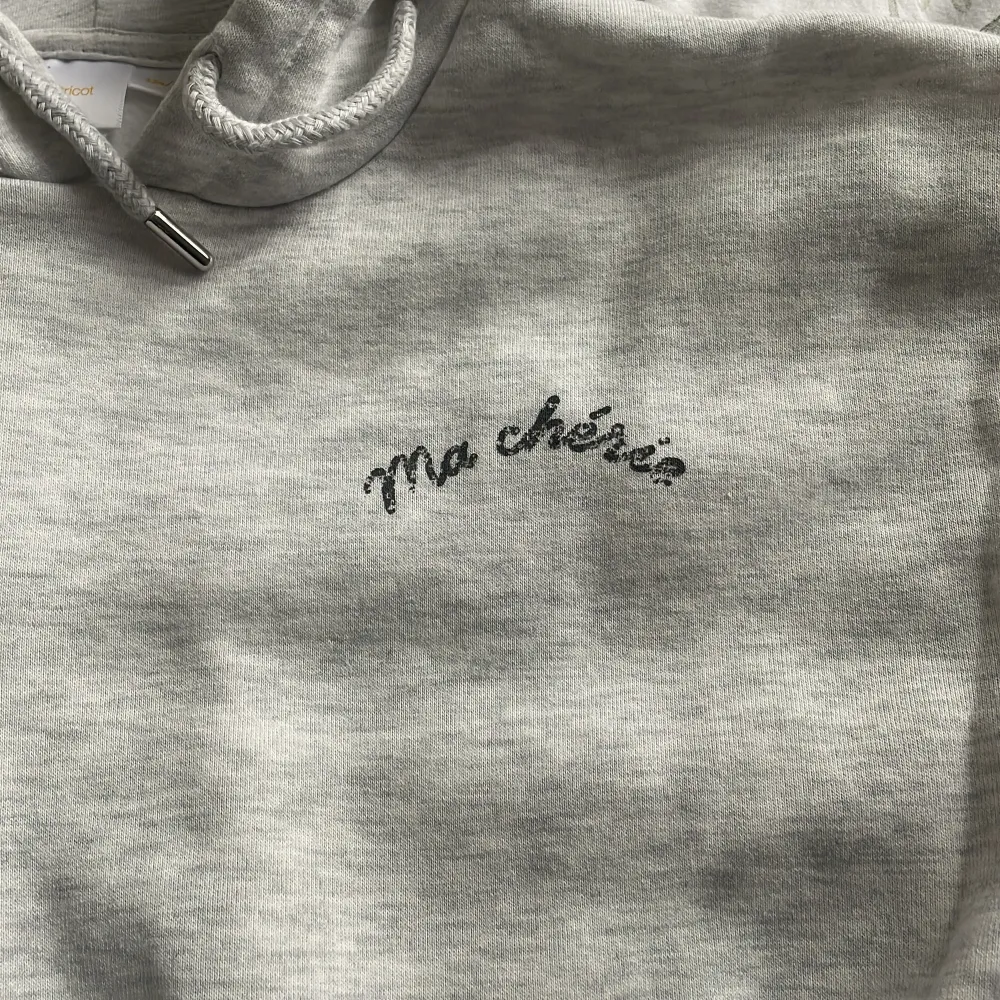 Säljer en supermysig grå hoodie från Gina Tricot med texten 'Ma chérie' i svart på bröstet och ett hjärta med samma text på ryggen. Perfekt för en chill dag eller när du vill vara bekväm men ändå snygg. Den har en klassisk huva och ribbade muddar vid ärmslut och nederkant. Passar perfekt till höst och vår!. Tröjor & Koftor.