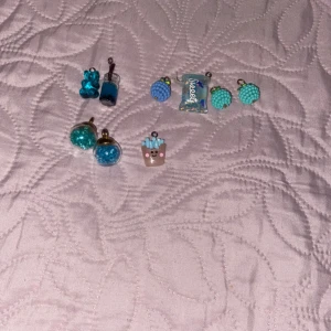 Färgglada örhängen med olika motiv - Säljer ett set med unika och färgglada örhängen. Det finns flera olika motiv, inklusive en blå nallebjörn, en blå flaska, och en söt liten figur med en krona. Perfekta för att ge en lekfull touch till din outfit!