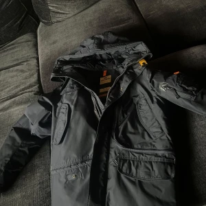 Marinblå jacka från Parajumpers - Säljer en marinblå Parajumpers jacka i mycket bra skick. Den har en stilren design med dragkedja och knappar, samt flera praktiska fickor. Perfekt för höst och vinter med sin varma och tåliga konstruktion. Jackan är långärmad och gjord i slitstarkt material. Passar både till vardags och mer äventyrliga aktiviteter.