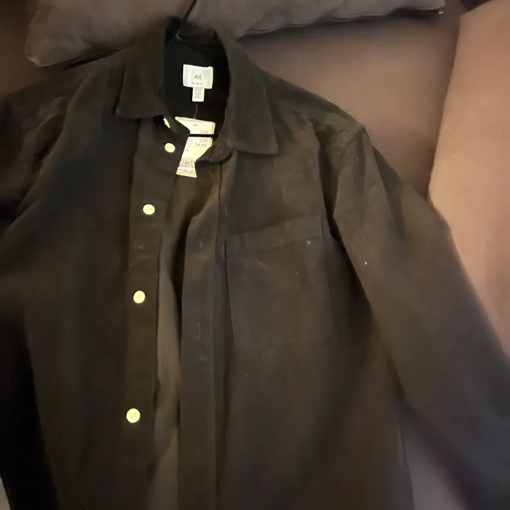 Säljer en stilren svart overshirt från H&M i mycket bra skick. Den har långa ärmar och knappar framtill. Perfekt för höst och vår, och funkar både till vardags och fest. Materialet känns mjukt och bekvämt, vilket gör den lätt att matcha med olika outfits. Helt ny . Skjortor.