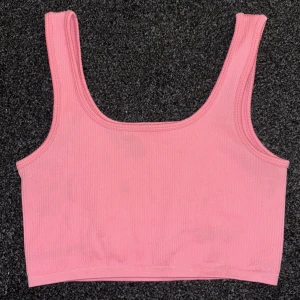 Rosa ribbad linnetopp - Säljer en söt rosa ribbad linnetopp i bra skick. Toppen är ärmlös och har en fyrkantig halsringning. Perfekt för sommardagar eller som ett lager under en jacka. Den är enkel och stilren, vilket gör den lätt att matcha med olika outfits. Dock har den en svart fläck på framsidan. 