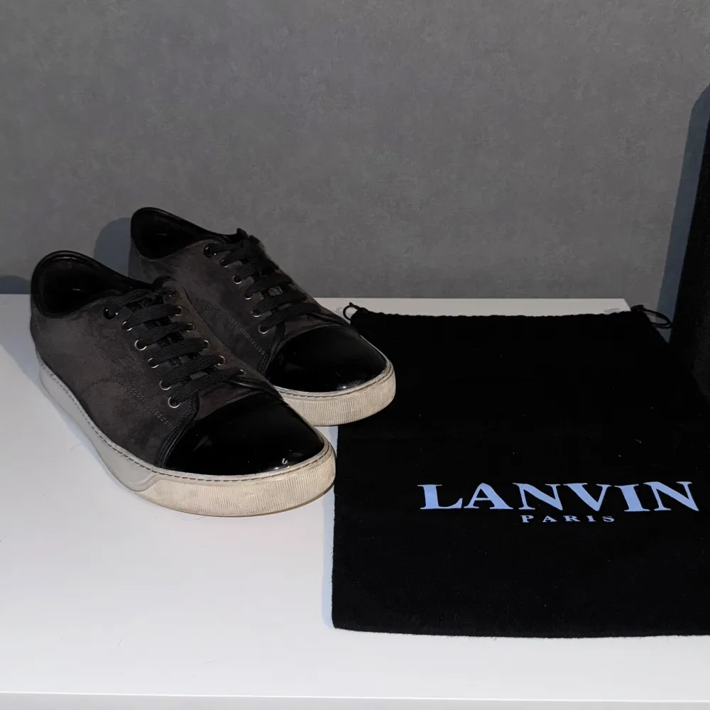 Säljer ett par stilrena svarta sneakers från Lanvin. De har en snygg kombination av mocka och lackdetaljer på tån. Skorna har en vit sula som ger en cool kontrast. Perfekta för både vardag och fest! Kommer med originalpåse.. Skor.