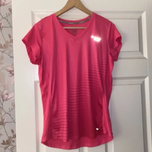 Rosa Dri-Fit t-shirt från Nike - Säljer en snygg rosa Dri-Fit t-shirt från Nike, perfekt för träning. Den har en v-ringad hals och korta ärmar. Materialet är lätt och andas bra, vilket gör den idealisk för intensiva pass. Reflekterande detaljer för extra synlighet. Passar perfekt för löpning eller gymmet! Den är liten i storleken så passar M och L.