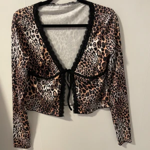 Leopard topp - Säljer en snygg leopardmönstrad bolerotopp med svarta spetsdetaljer. Toppen har långa ärmar och en knytning framtill. Perfekt för en utekväll eller fest! 🐆✨