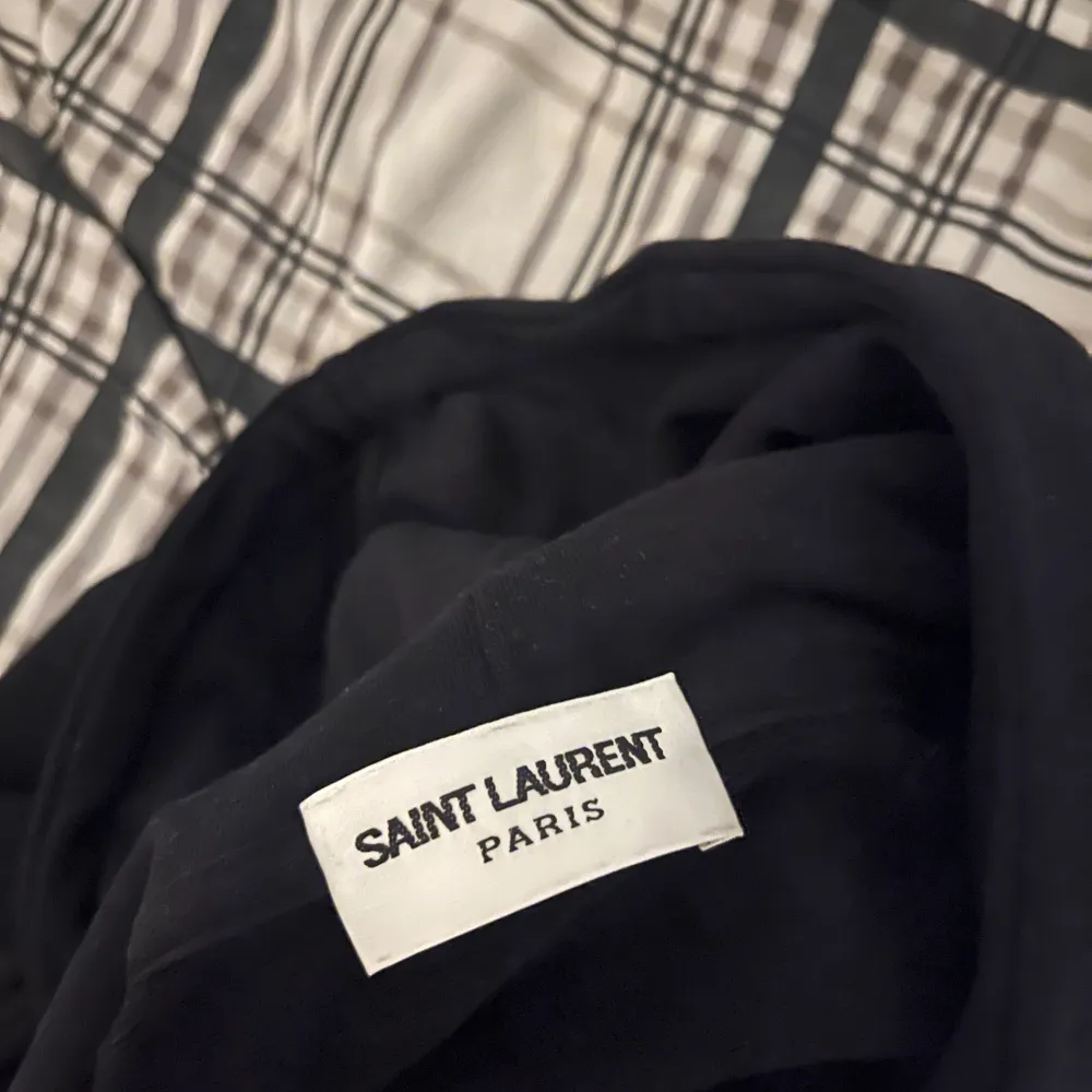 Säljer en snygg svart hoodie från Saint Laurent med deras ikoniska logga i vitt på framsidan. Den är i storlek M, men sitter mer som en S. Skick 9/10 då den är välvårdad och skonsamt använd. Vid frågor är det bara att skriva!. Hoodies.