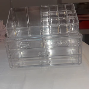 Transparent sminkförvaring - Säljer en superpraktisk transparent sminkförvaring med flera fack och lådor. Perfekt för att organisera allt ditt smink som läppstift, ögonskugga och borstar. Den är gjord av akryl och har en stilren design som passar alla rum. Perfekt för att hålla ordning på sminkbordet!