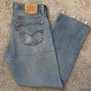 Levi's 501 jeans i ljusblå denim - Säljer ett par klassiska Levi's 501 jeans i ljusblå denim. De har en rak passform och är i bra skick med snyggt slitna kanter vid bensluten. Perfekta för en avslappnad stil och funkar året runt. Passar både till vardags och fest. 🕺🏼