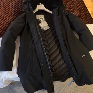 Svart vinterjacka från Woolrich - Säljer en svart vinterjacka från Woolrich i mycket bra skick. Jackan har en långärmad design med dragkedja och knappar. Den är perfekt för kalla vinterdagar med sin varma vaddering och stilrena look. Passar både till vardags och mer uppklädda tillfällen.
