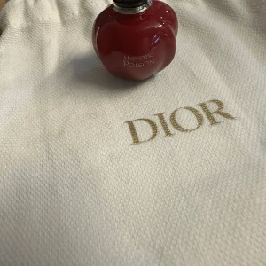Hypnotic Poison Eau de Toilette från Dior - Säljer en elegant och förförisk Hypnotic Poison Eau de Toilette från Dior. Flaskan är röd och formad som ett äpple med en svart kork. Perfekt för den som vill ha en doft som sticker ut. Kommer med en vit påse med Dior-logga.