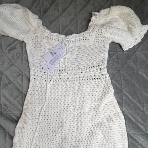 Vit stickad klänning - Säljer en superfin vit stickad klänning med korta puffärmar och en söt knytning framtill. Perfekt för sommarens på tex stranden. Klänningen är i storlek S men tyckte den var något större till storleken💕