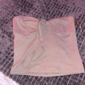 Beige tubtopp från Gina Tricot - Säljer en snygg beige tubtopp från Gina Tricot i storlek M. Toppen är axelbandslös och har en enkel design med en liten knytning framtill. Perfekt för sommardagar eller en utekväll. Materialet känns mjukt och bekvämt mot huden.