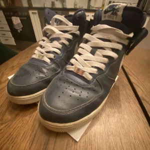 Blå Nike Air Force sneakers - Säljer ett par klassiska blå Nike Air Force sneakers i bra skick. De har en snygg vit sula och vita snören som ger en fräsch look. Perfekta för vardagsbruk och nu i vinter. Storlek US 8.5, vilket motsvarar herr 42 i EU-storlek. 