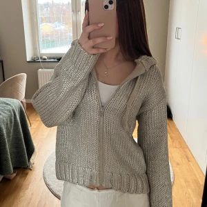 Silvrig  stickad hoodie från Zara - Mysig silvrig stickad hoodie från Zara i storlek S. Perfekt för kyliga dagar med dragkedja och huva. Den har en avslappnad passform och ribbade muddar vid ärmslut och nederkant. Superfin att matcha med jeans eller leggings för en casual look.
