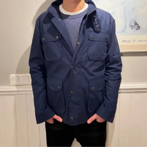 Fieldjacket mörkblå - Säljer en stilren mörkblå jacka med knappar framtill. Den har fyra fickor med lock och knappar. Jackan är långärmad och har en klassisk krage. Passar både till vardags och lite finare tillfällen.