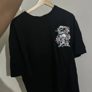 Svart t-shirt med tryck från SMOG - Cool svart t-shirt från SMOG med ett stort tryck på ryggen. Trycket har texten 'Dark Spirit' och 'Life is Short, Death is Forever' med en dödskalle, blommor och en orm. Perfekt för en avslappnad stil med en edgy touch. T-shirten är i bomull och har en relaxed fit.