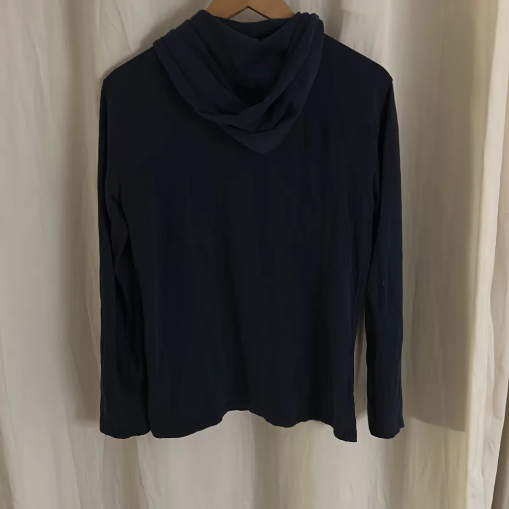 Säljer en stilren mörkblå hoodie från Ralph Lauren i storlek XS. Den har en klassisk design med en liten röd logga på bröstet och justerbara snören i huvan. Perfekt för både vardag och avslappnade tillfällen. Skön och enkel att matcha med det mesta! 💙. Neuletakit & Villapaidat.