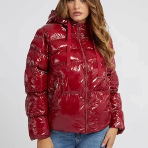 Glansig röd pufferjacka från Guess - Säljer en glansig röd pufferjacka från Guess. Den är perfekt för kalla dagar med sin varma vaddering och har en dragkedja framtill.  Är i mycket bra skick. Perfekt för vintern! säljer pågrund av att den inte kommer till användning.
