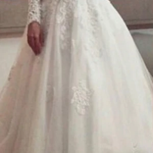 Vit brudklänning med spetsdetaljer - Underbar vit brudklänning med långa spetsärmar och vackra broderade detaljer. Klänningen har en elegant lång design med en voluminös kjol som ger en sagolik känsla. Perfekt för bröllop och speciella tillfällen. Den har en klassisk och tidlös stil som passar alla säsonger.