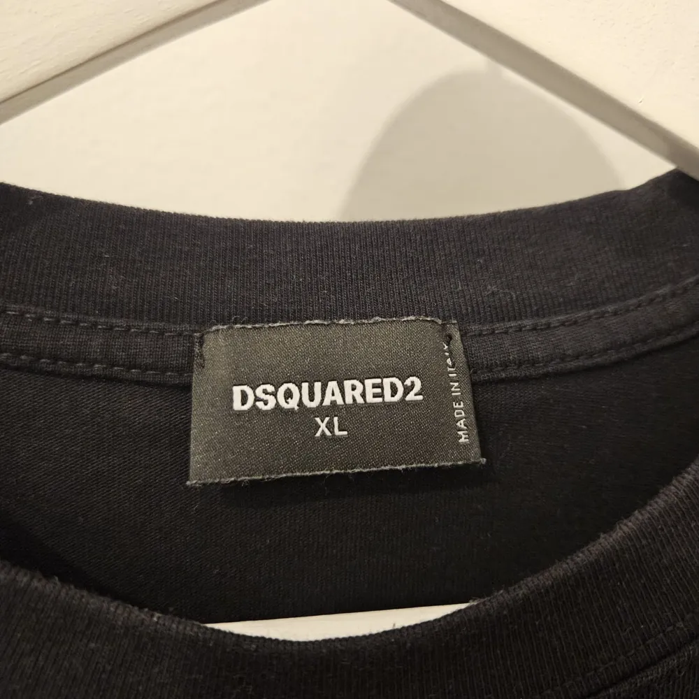 Säljer en svart t-shirt från Dsquared2 i storlek XL. Den har en cool text 'ICON' i rosa och orange med palmträdsmönster. Perfekt för en avslappnad stil eller fest. T-shirten är i mycket bra skick och gjord av mjukt material. OBS LITEN I STORLEK SIZE SITTER SOM STORLEK L. T-shirts.