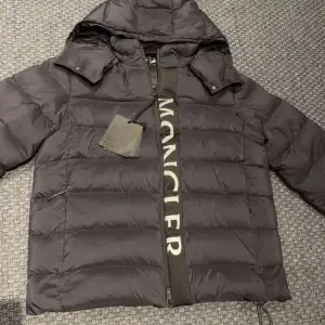 Säljer en snygg svart dunjacka från Moncler i mycket bra skick. Jackan har en avtagbar huva och dragkedja framtill. Perfekt för kalla vinterdagar med sin varma och puffiga design. Moncler-loggan syns tydligt på ärmen. Passar både till vardags och lite finare tillfällen.