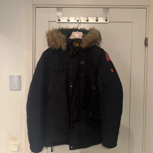 Mörkblå vinterjacka från Parajumpers - Säljer en svart Parajumpers vinterjacka med pälsfodrad huva. Jackan har en cool patch på ärmen och praktiska fickor. Perfekt för kalla dagar! Barn storlek men är väldigt stor i storleken. Passar som en S/M. Pris inte hugget it sten! Skriv för fler bilder eller frågor.