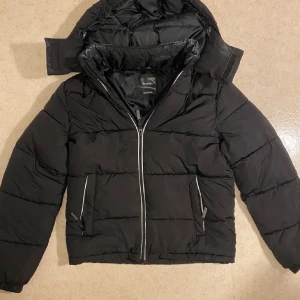 Svart pufferjacka från Bershka - Säljer en svart pufferjacka från Bershka i storlek XS. Jackan har en dragkedja framtill och är perfekt för kalla dagar. Den är i mycket bra skick och har en stilren design med långa ärmar och en mysig huva. Perfekt för höst och vinter!