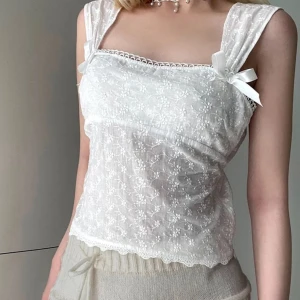 Vit spetslinne med rosetter - Säljer ett superfint vit spetslinne med söta rosetter på axelbanden. Toppen är ärmlös och har ett vackert blommigt mönster💓